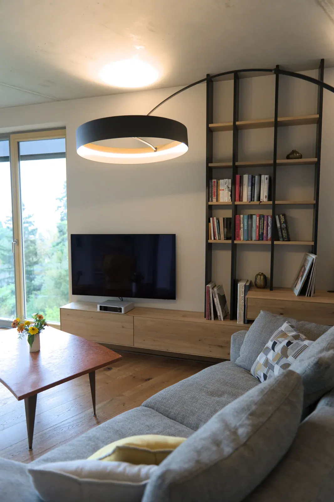 Wohnzimmer mit grauem Sofa, Holzregal, TV-Möbel und schwarzer Ringleuchte